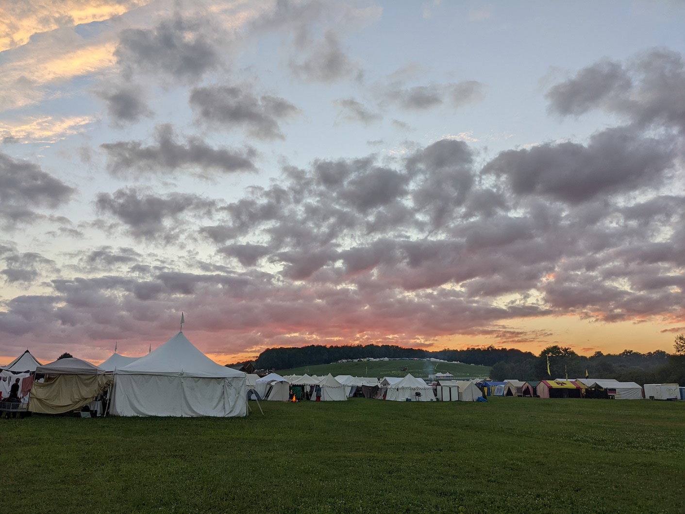 similar sky but more of the color at the horizon is visible behind a row of tents; a small fire is lit in front of one of them